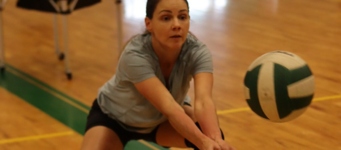 Adult athlete practicing volleyball passing with USSPT coach in gym, focusing on form and skills development.