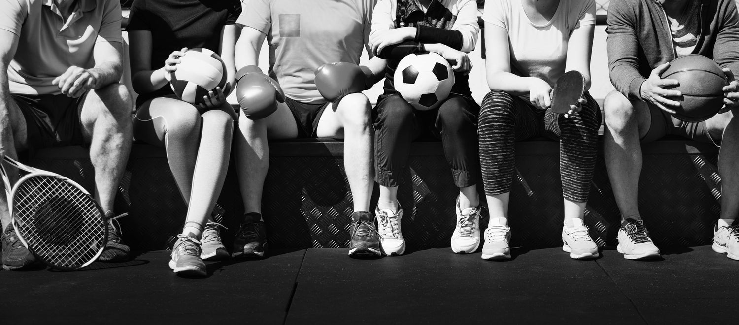 Group of adult athletes with sports gear like volleyball, soccer ball, and tennis racket, showcasing multi-sport training at USSPT